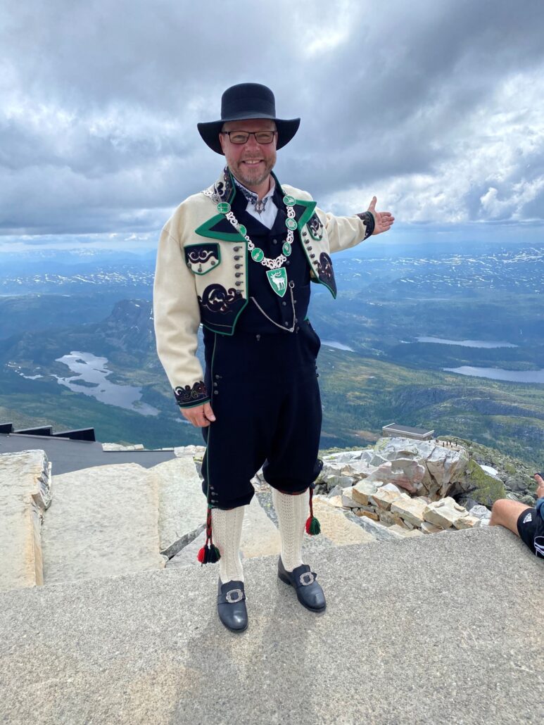 Bilde av ordføreren som peker mot kommunen sin fra en fjelltopp.